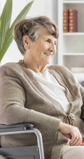 Bild einer fröhlichen Seniorin im Rollstuhl, im Hintergrund unterhalten sich zwei ältere Herren