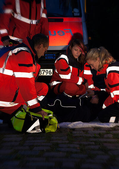 Bild eines Rettungsdienst Teams im Einsatz bei Nacht, die Rettungsdienstkleidung reflektiert gut sichtbar.